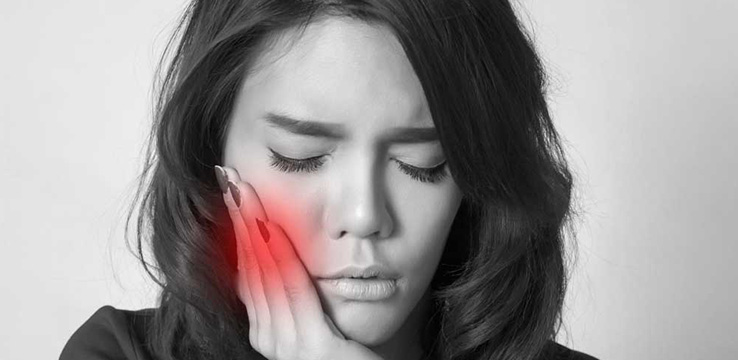 black and white a woman holds her cheek which is in red signifying that she is in pain