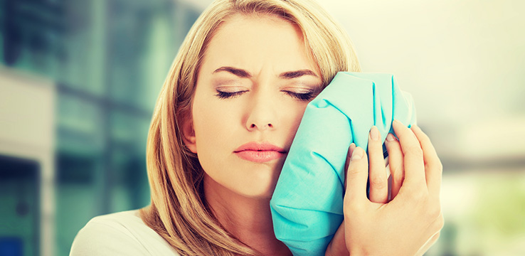 woman holding an icepack to her face with her eyes closed