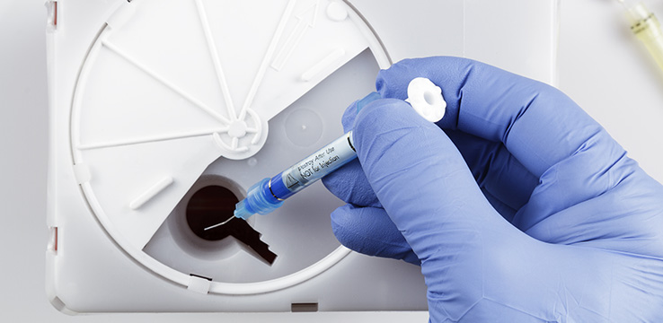 an image of a gloved hand dropping a medical syringe into a safe box