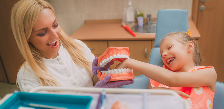 female dentist and a young girl is laughing while putting her hand in to dental gypsum model