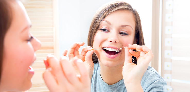 beautiful teenage girl flossing her teeth at home