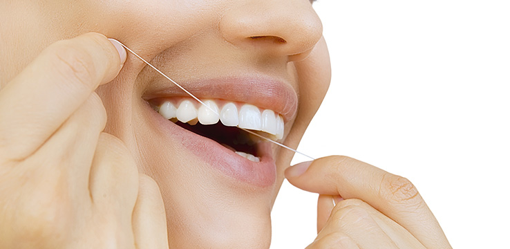 close up of woman's mouth as she uses dental floss on her top teeth.