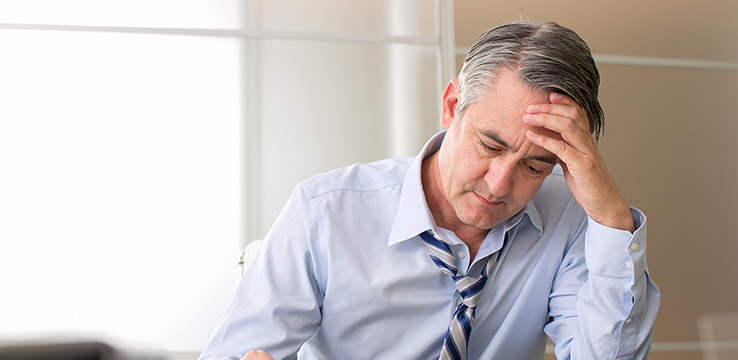 older man looking disheveled holding his head and looking down