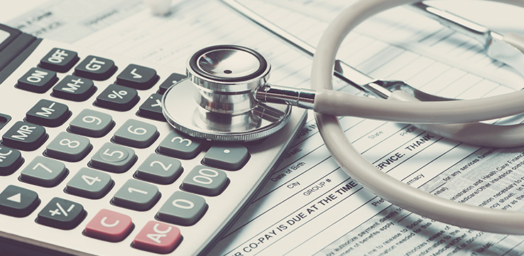 papers on a desk with a calculator and a stethoscope on top of them.