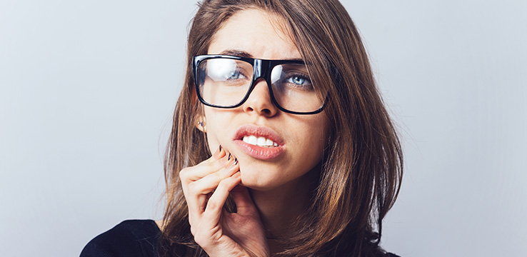 woman wearing huge glasses pushing on her jaw as if it hurts