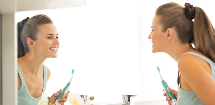 young woman looking pleased as she checks her teeth in the mirror she is holding a tooth brush